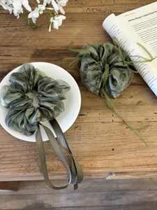 Detail van bosgroene organza scrunchies met lange linten op een houten ondergrond