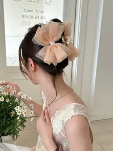 Élégante pince à cheveux en mesh champagne avec nœud et perles montrée sur modèle.