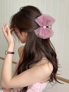 Détail d'une pince à cheveux nœud en résille rose avec perles sur cheveux bruns.