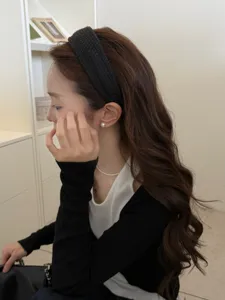 Asian woman wearing a stylish wide black woven headband in a minimalist indoor setting