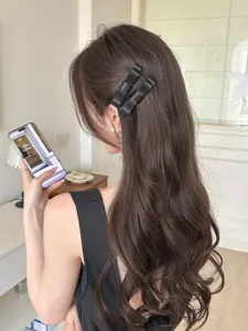 Detailansicht eleganter schwarzer Satin-Schleifen-Haarspangen in langem gewelltem Haar.