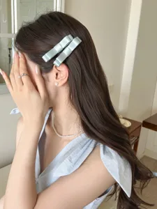 Detailaufnahme eleganter hellgrüner Satinschleifen-Haarspangen auf braunem Haar