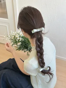 Elegante Detailansicht von zwei hellgrünen Satin-Schleifen-Haarspangen im Zopf.