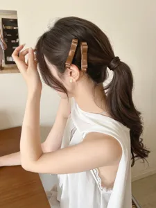 Detailansicht einer eleganten braunen Satin-Schleifen-Haarspange im Haar einer Frau.