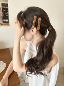Detailansicht von zwei braunen Satin-Haarspangen in elegantem, gewelltem Haar.