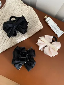 Elegant satin bow hair claws with rhinestones displayed on a textured fabric surface