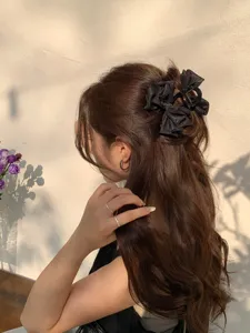 Detailed view of elegant black satin bow hair claw clip with rhinestones in wavy hair