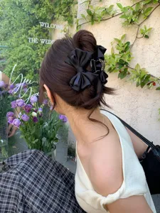 Elegant black satin bow hair claw with subtle rhinestones shown on a half-up hairstyle.