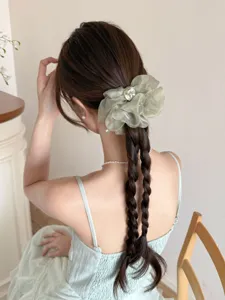 Gros plan d'un chouchou en maille vert sauge avec bouton sur cheveux tressés