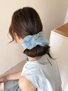 Gros plan d'un chouchou en maille bleu clair porté sur un chignon bas élégant.