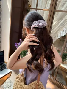 Detalle de un pasador de pelo tipo banana con lazo plisado morado en cabello ondulado.