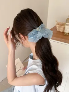 Détail d'un chouchou en tulle bleu clair sur la queue de cheval d'une femme aux cheveux bruns