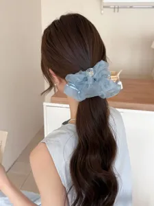 Détail d'un chouchou en maille bleu clair avec nœud et bouton transparent sur un élastique