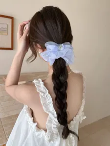 Gros plan détaillé d'un chouchou nœud en organza bleu clair sur une longue tresse.