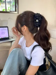 Detalle de un elegante clip de pelo banana negro plisado con gema de corazón en una coleta