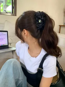 Primer plano de un clip de pelo tipo banana negro con volantes y un corazón de cristal