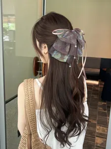 Close-up detail of a fairy mesh bow hair clip with dangling charms on wavy brunette hair