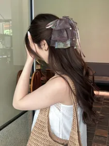 Detailed side view of a brown tie-dye mesh bow hair clip with silver charms
