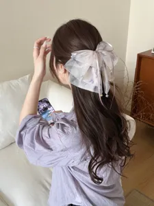 Detail view of an elegant purple mesh bow hair claw clip with pearl accents on long wavy hair.