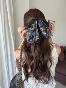 Detail view of an elegant floral mesh bow hair clip styled on long wavy brown hair