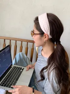 Asian model wearing a pink polka dot wide headband while working on a laptop at home.