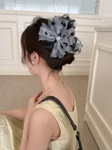 Detail view of a grey mesh polka-dot bow shark clip with pearl center on hair.