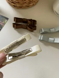 Detailansicht der Metall-Entenschnabel-Haarspange und des Satinstoffs der Schleife.