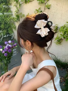 Detailed view of an elegant cream satin bow hair claw clip with rhinestone accents