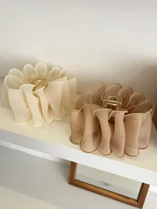 Détail rapproché de grandes pinces à cheveux en maille plissée crème et marron sur étagère