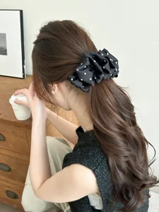 Detailed view of an elegant black polka dot bubble hair clip on wavy brown hair.
