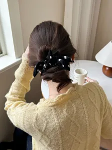 Close-up view of a black polka dot bow scrunchie styled on a brunette hair bun.