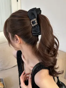 Close-up of black satin bow banana clip with square crystal buckle on a wavy ponytail