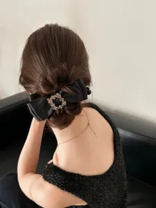 Elegant black satin bow hair clip with a rhinestone square buckle shown on a bun