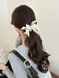Detailed view of a white polka dot bow scrunchie securing a wavy ponytail hairstyle