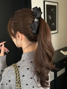 Close-up of an elegant black bow banana hair clip with a rhinestone buckle on a ponytail