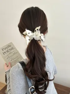 Detailed view of a sweet white polka dot bow scrunchie styled on a brunette ponytail.