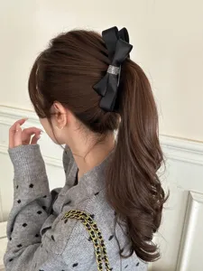 Detail shot of a black satin bow banana clip with rhinestones worn in a ponytail.