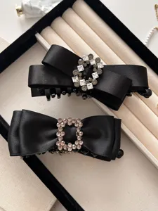 Close-up of two elegant black satin bow hair clips with sparkling rhinestone buckles