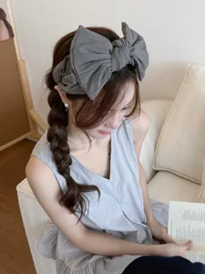 Détail d'un grand serre-tête à nœud en tissu gris anthracite sur les cheveux tressés.