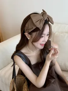 Détail élégant d'un grand bandeau à nœud marron uni avec bord large sur un modèle.