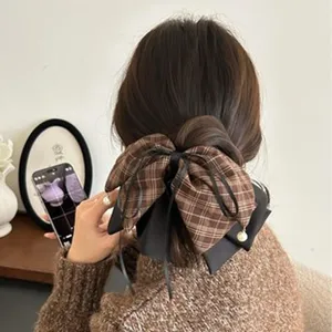 Gros plan d'une pince à cheveux à nœud écossais marron avec ruban en satin noir.