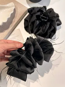 Close-up of a large black satin bow claw clip with feathers and glitter details