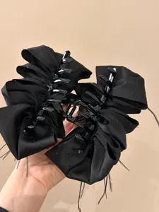 Close-up detail of a large black satin bow hair claw clip with feathers and sequins