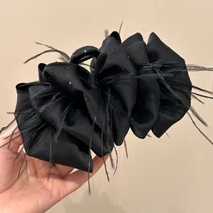Large black bow hair claw with feather and sparkle detail for elegant styling.