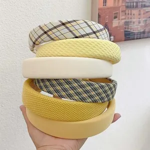 Gros plan de serre-têtes rembourrés empilés en jaune, crème et motifs à carreaux.
