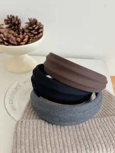 Primo piano di tre cerchietti larghi in tessuto a righe nei colori marrone, nero e grigio.