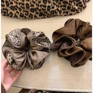 Close-up van bruine en champagne zijden scrunchies met luipaardprint splicing details.