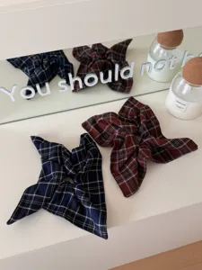 Detailed macro view of plaid bow hair scrunchies in navy and brown on a white vanity.