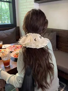 Close-up of a ruffled bow hair clip worn by a woman in a cozy cafe setting.