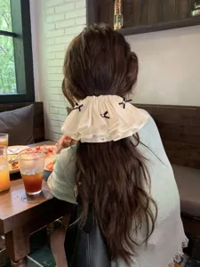 Elegant cream ruffled bow hair clip shown on model in a cafe setting for half-up hair
